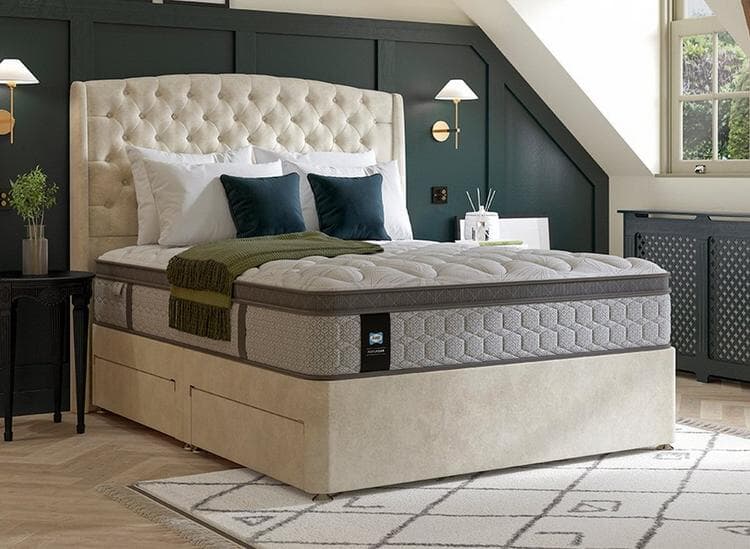 A light cream bed frame in the centre of a bedroom with dark green wall panelling. Light comes in through a sash window to the right.