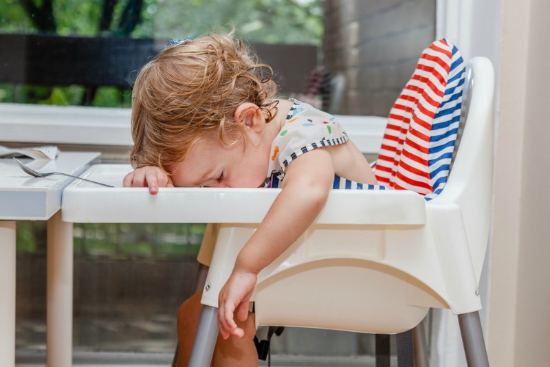 A young child is asleep in a white baby feeding chair