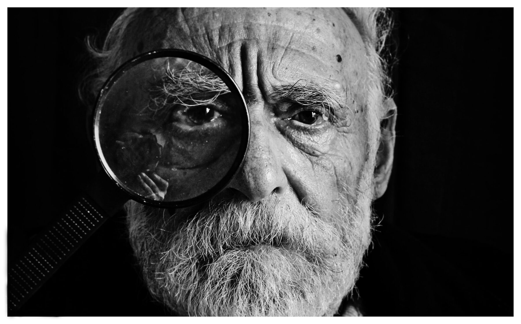 close up facial portrait of an elderly gent with a magnifying glass over his eye