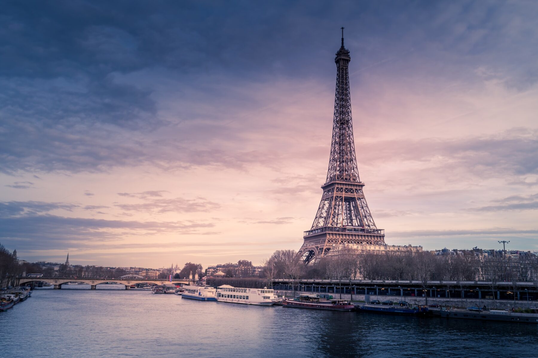 the river seine at dusk with the Eiffel Tower towering over the waters edge