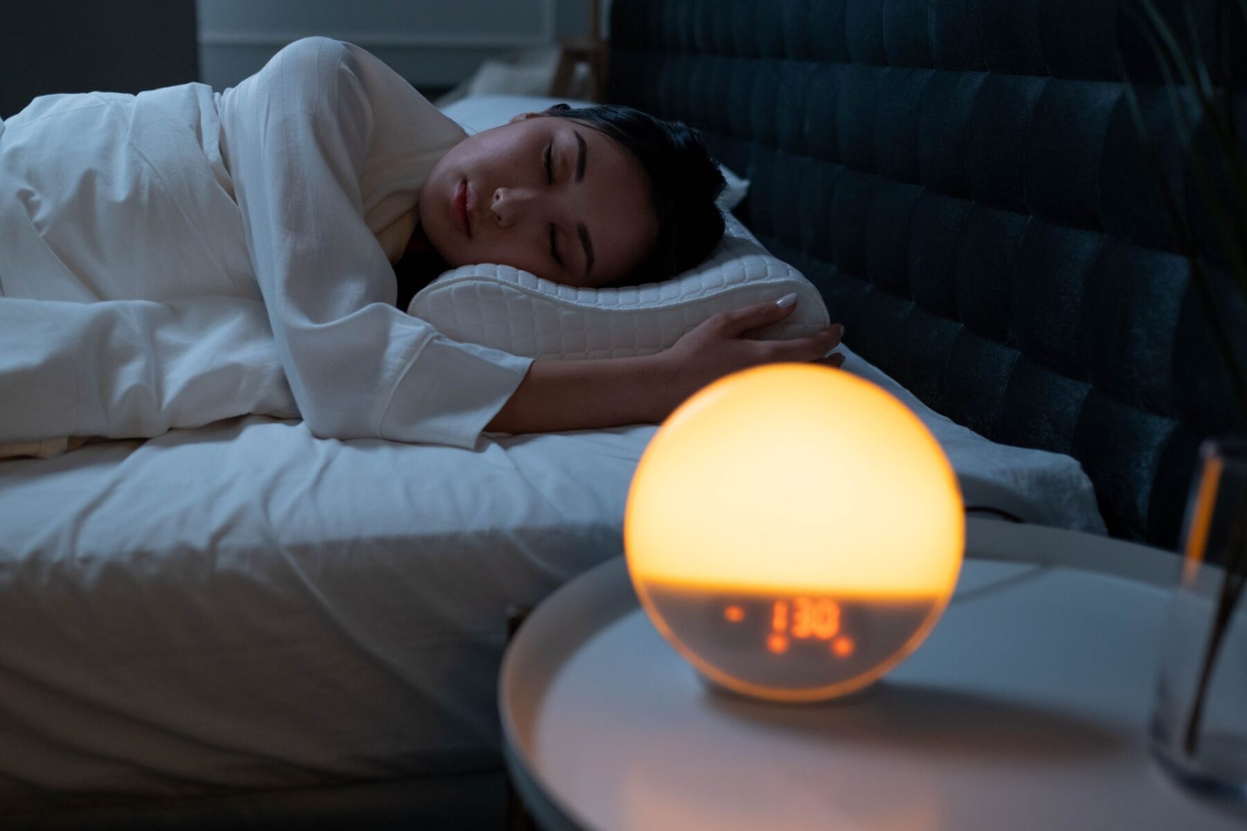 Woman sleeping peacefully in a cosy bedroom with ambient bedside light.